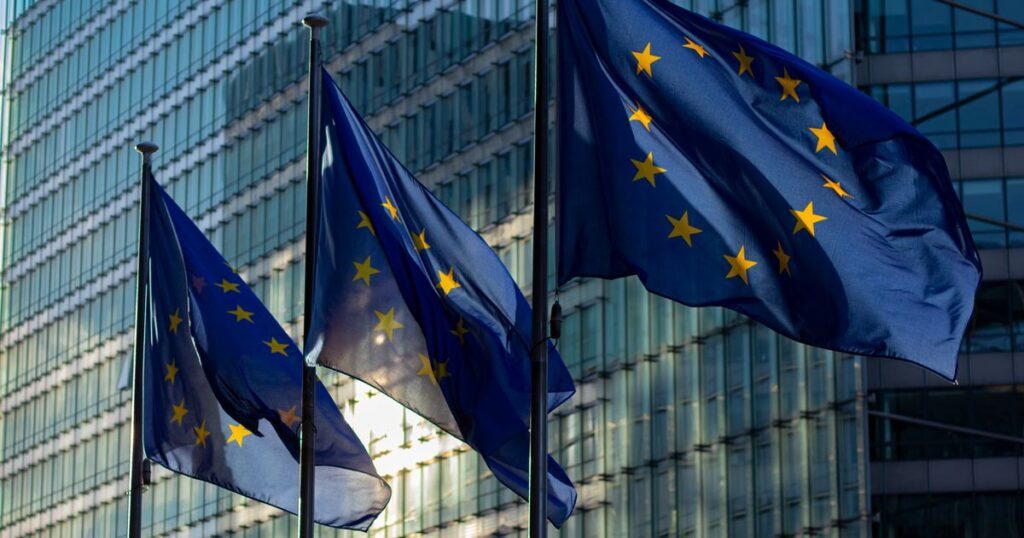 Bandiere dell'Unione Europea davanti a un edificio istituzionale in vetro — direttiva NIS2 dell'UE per le PMI